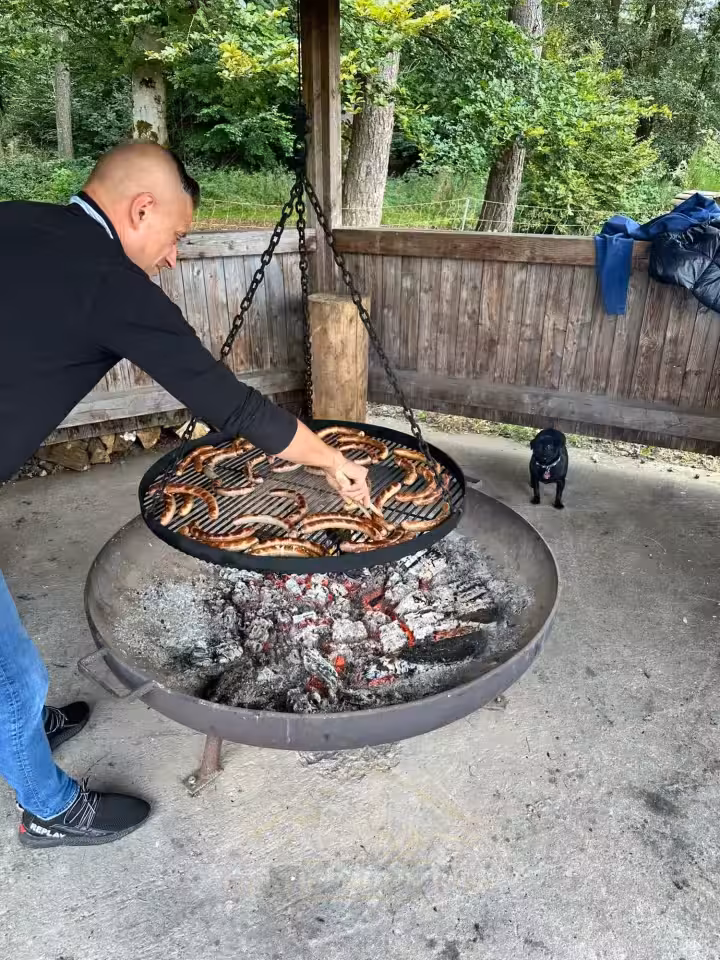 Gäste bereiten an der Feuerstelle gemeinsam Essen beim Mastiff- und Mops-Treffen 2024 zu.