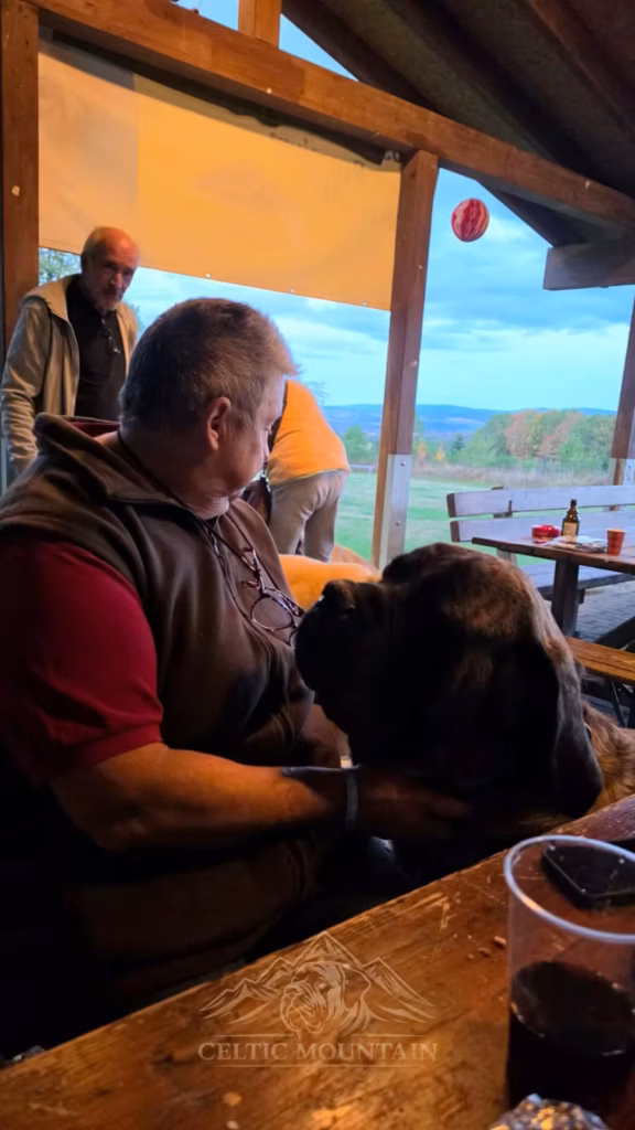 Ein sitzender Gast und ein dunkler Mastiff wenden sich in der Grillhütte einander zu.