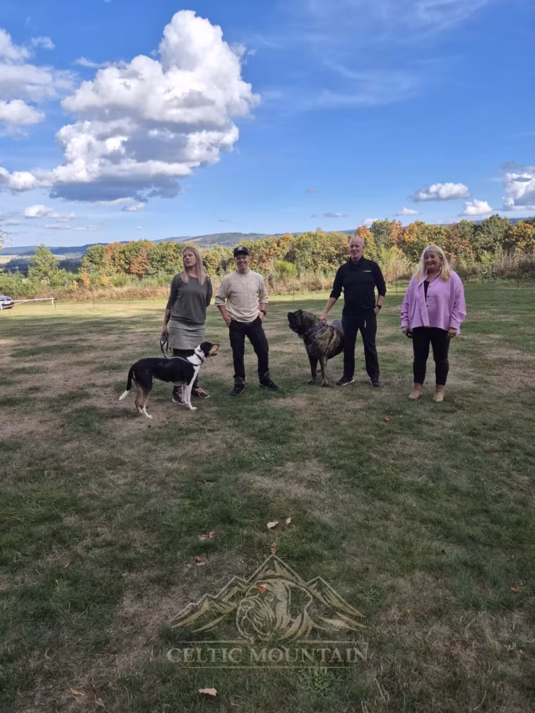 Vier Gäste stehen mit einem Mastiff und einem kleineren Hund auf der Wiese unter großen weißen Wolken.