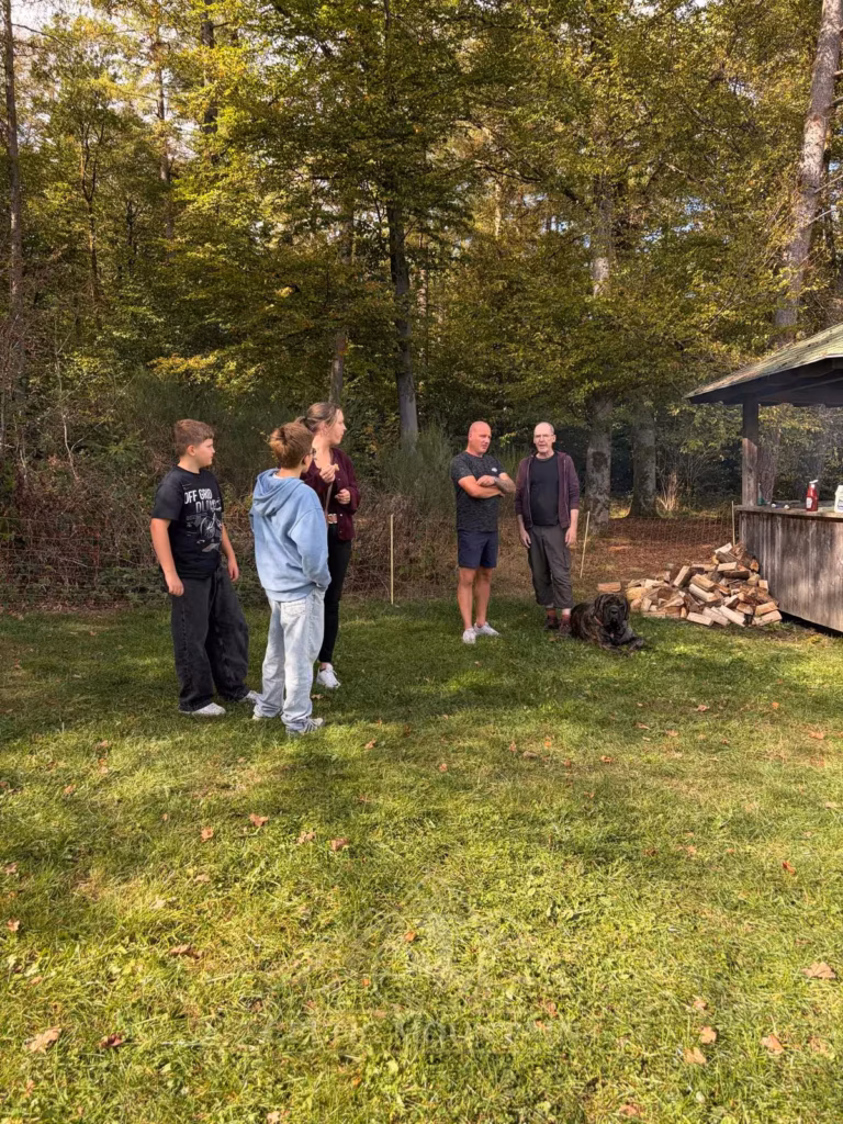 Vier Gäste stehen in einer kleinen Gesprächsrunde auf der Wiese vor herbstlichen Bäumen.