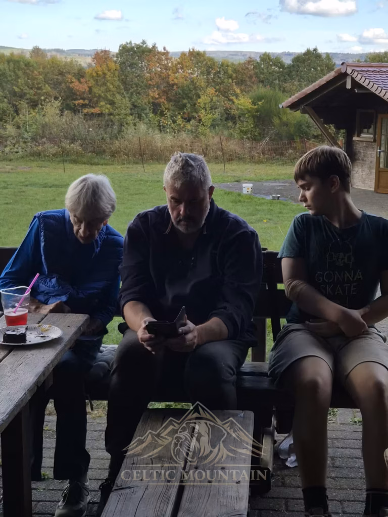 Drei Gäste sitzen nebeneinander auf einer Holzbank unter dem Dach der Grillhütte.