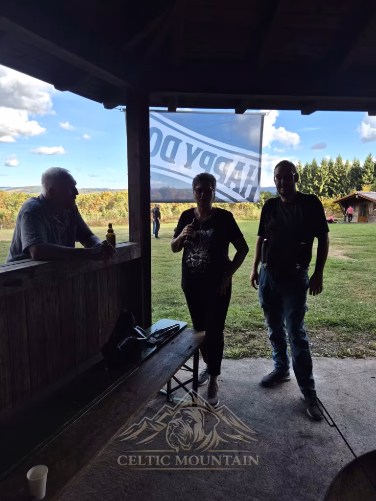 Drei Gäste stehen im Schatten des Pavillons; durch die offene Seite fällt der Blick auf die helle Wiese.