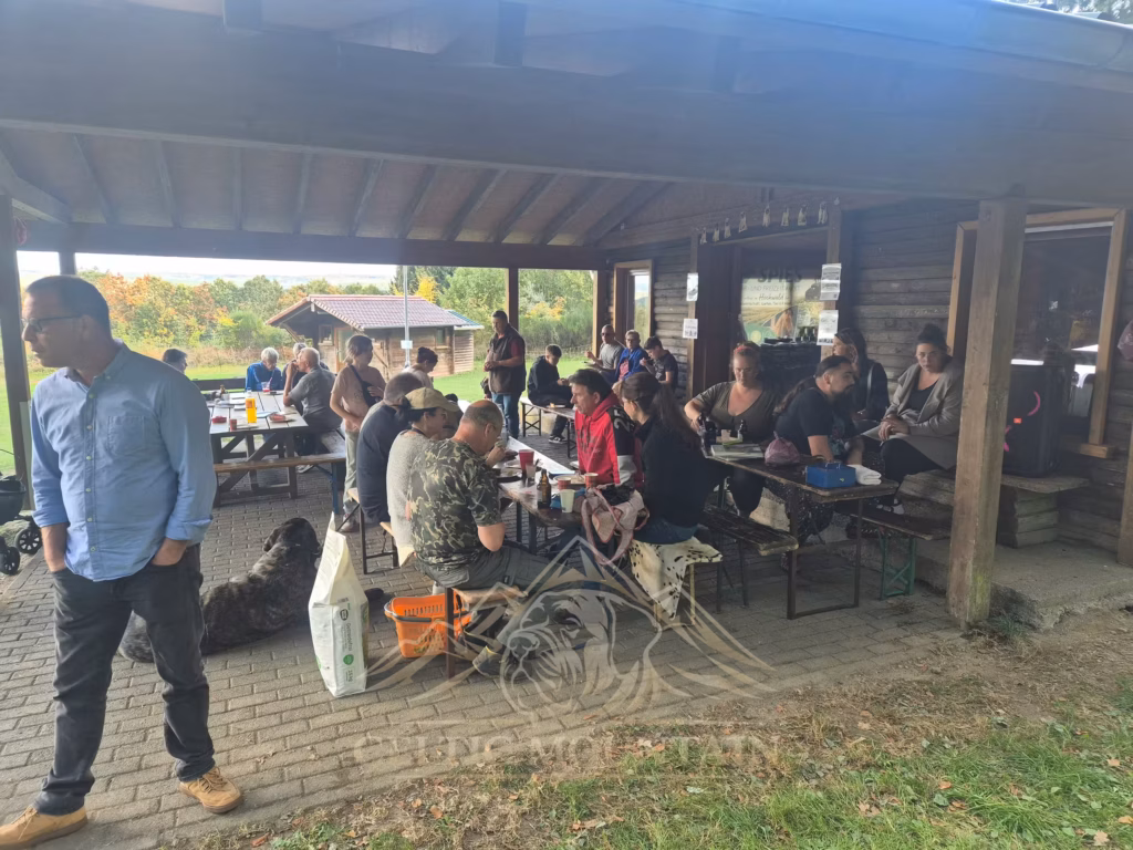 Viele Gäste sitzen an Biertischen in der offenen Grillhütte, während Mastiffs zwischen den Bänken stehen.