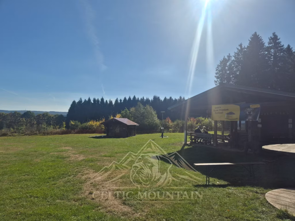 Die Sonne scheint über eine große Wiese mit hölzerner Grillhütte und Pavillon.
