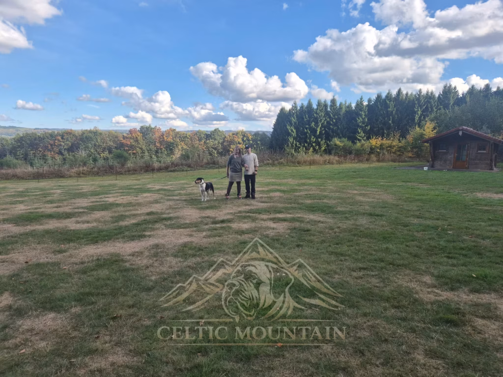 Zwei Gäste mit Hunden stehen auf einer großen Wiese unter blauem Himmel mit hellen Wolken.